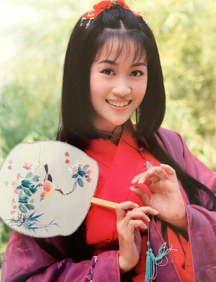 people-A-smiling woman-A-Asian traditional dress-A-holding a fan-A-outdoor setting