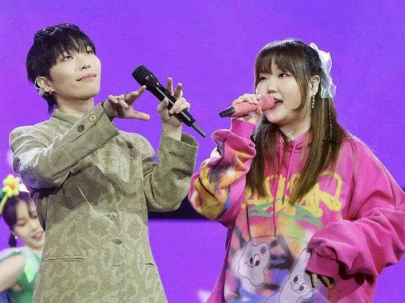 people-Two singers performing on stage-A-male singer-A-tan patterned mandarin collar jacket-B-female singer-B-bright pink tie-dye hoodie-C-purple background