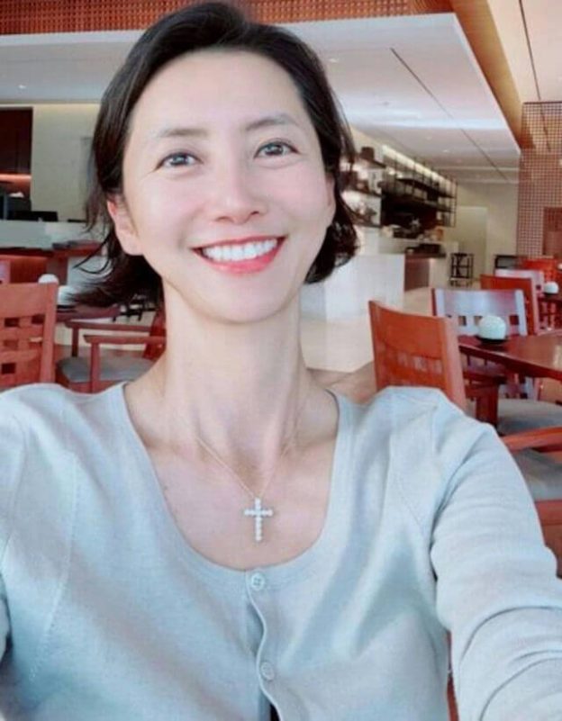 people-1-woman-A-smiling-A-cross necklace-A-light blue cardigan