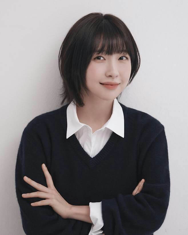 people-woman-A-short black hair-A-bangs-A-white collared shirt-A-dark blue v-neck sweater-A-smiling-A-arms crossed