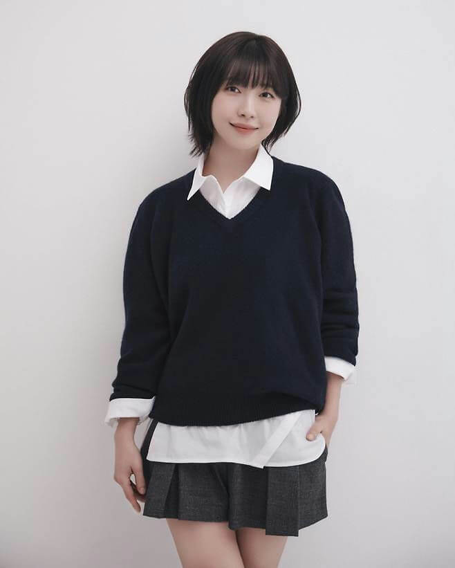 people-A-woman-A-short black hair-A-V-neck navy sweater-A-white collared shirt layered-A-grey pleated shorts