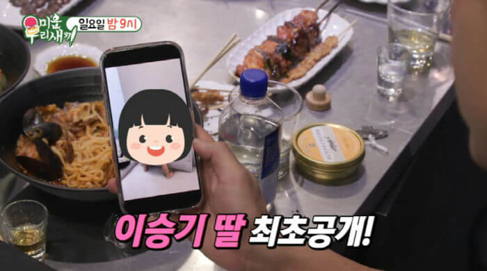 people-0-person holding phone-1-food on table-2-smartphone screen with cartoon-3-Korean text