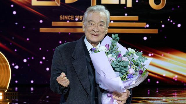 people-elderly Asian man-holding a bouquet-smiling-on stage-wearing a suit