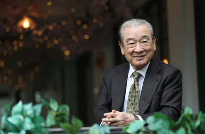 people-An elderly Asian man-A smiling man-A man wearing a suit and tie-A man seated outdoors with bokeh lights in the background