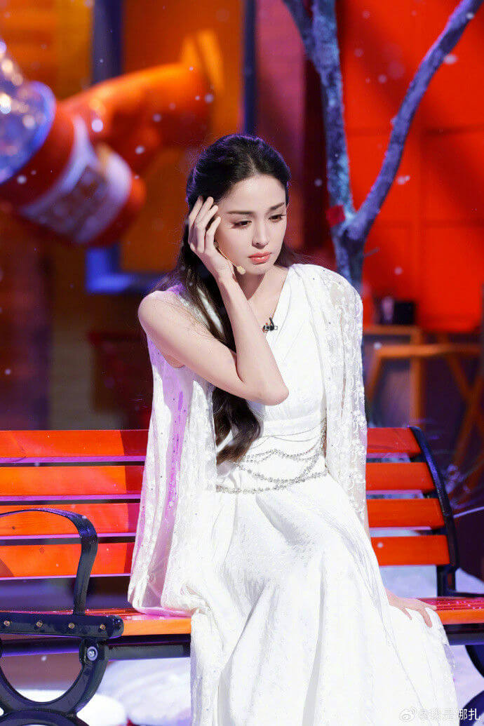 people-A-woman-A-sitting-A-white dress-A-on a bench-B-hand to head-B-long dark hair-C-stage setting-C-sparkling effect