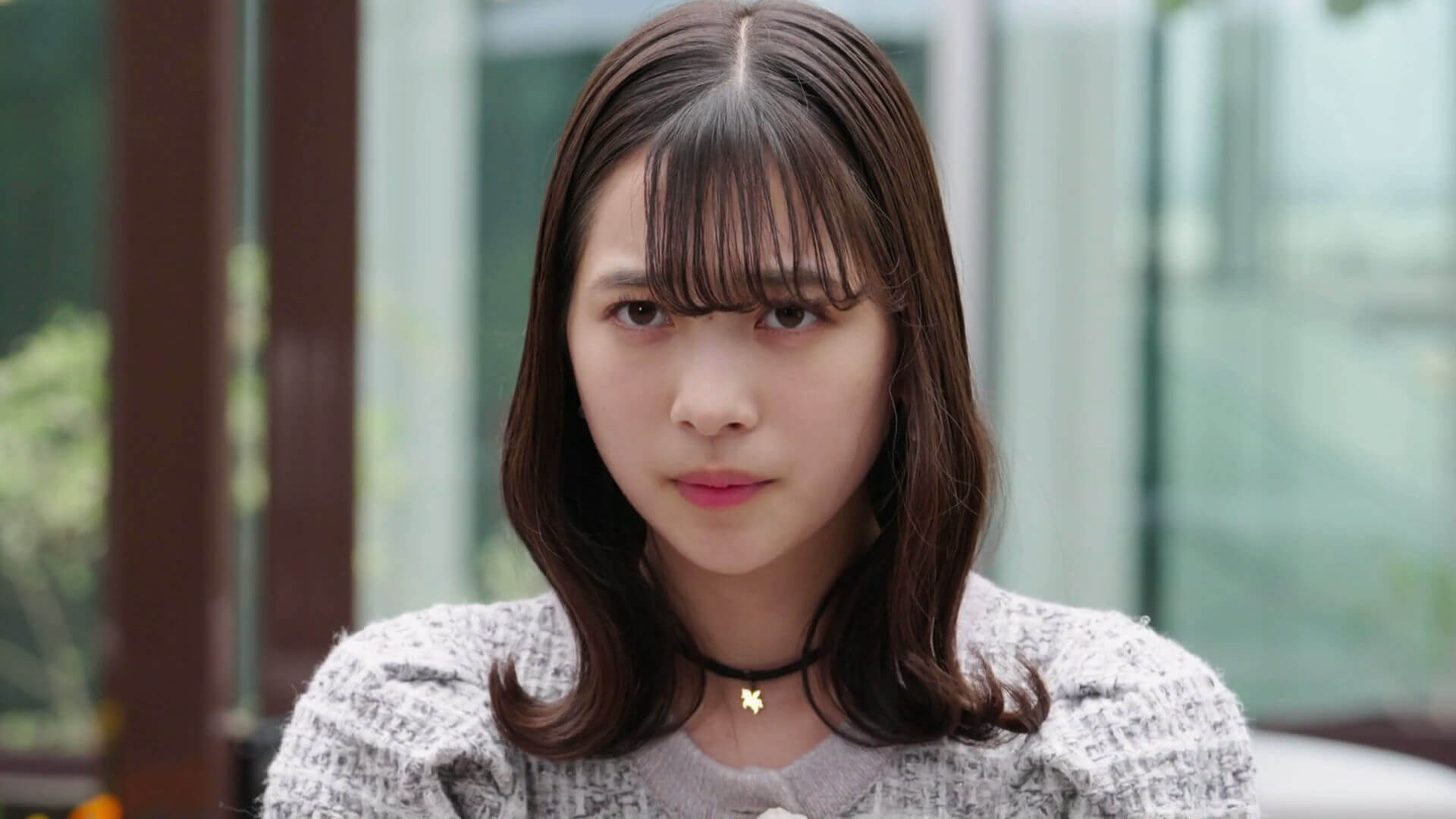 people-young woman-brown hair-bangs-black choker-gold star pendant-tweed jacket-serious expression