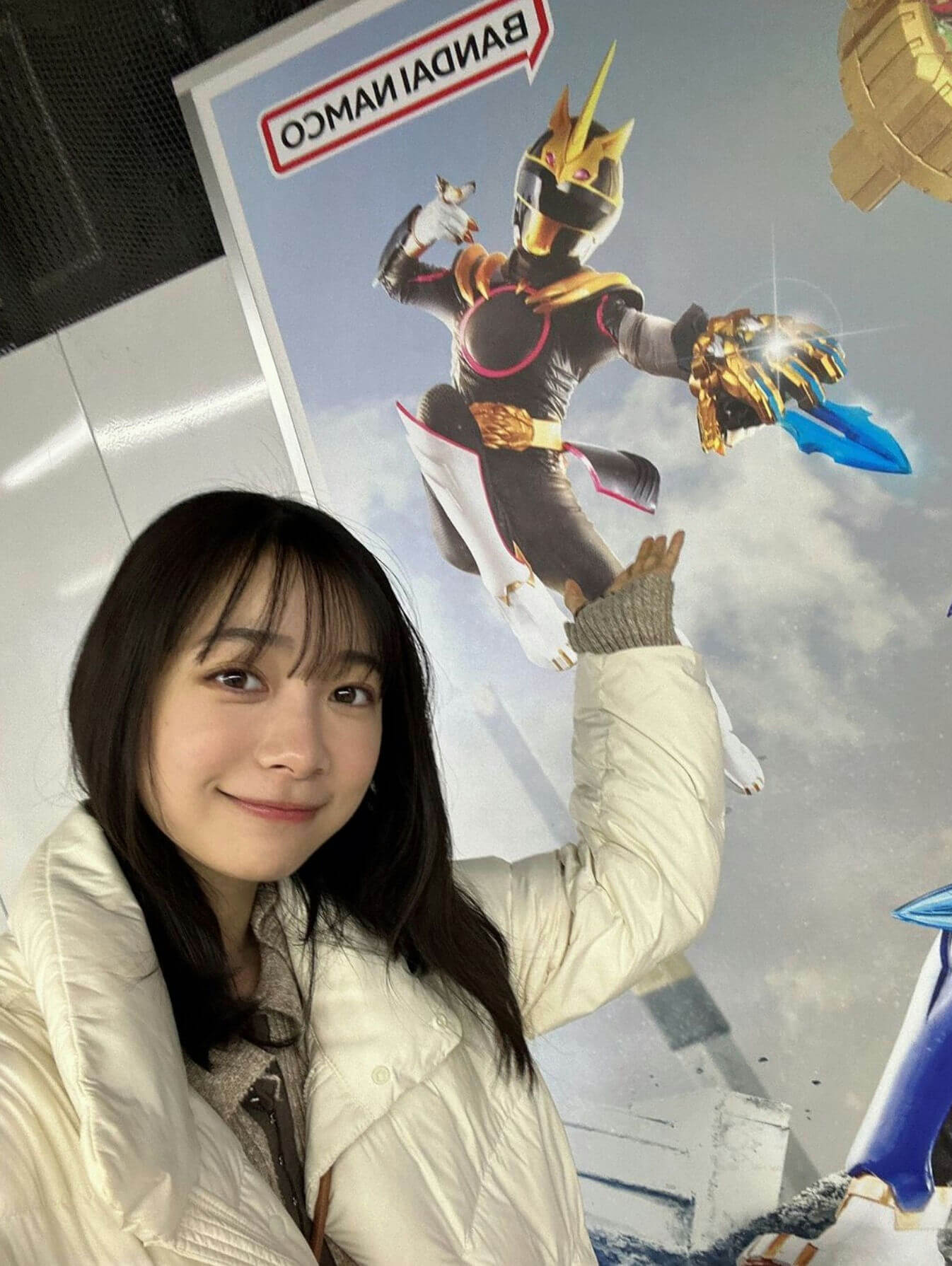 people-A-young woman-A-smiling-A-posing with hand up-B-holding up hand near a poster-C-standing in front of a promotional image