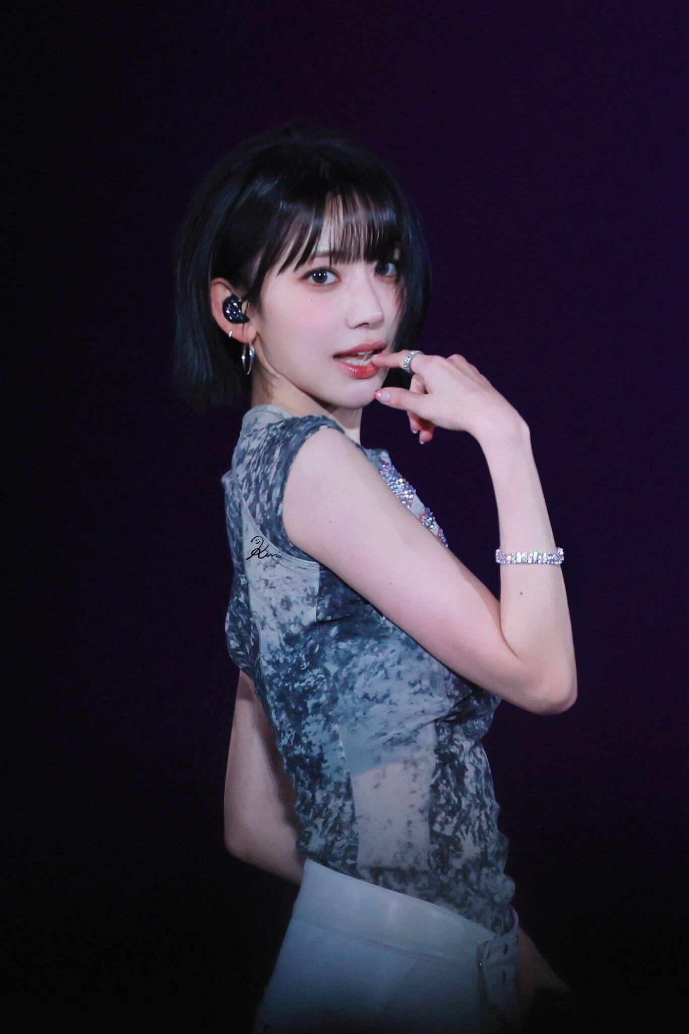 people-Sakura Miyawaki-performer-stage-dark background-short black hair-blue/grey patterned top-diamond bracelet