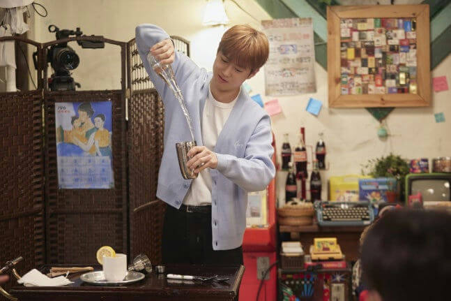 people-A-young man-A-bartender-A-mixing drink-A-light blue cardigan-B-pouring liquid-B-cocktail shaker-C-vintage interior
