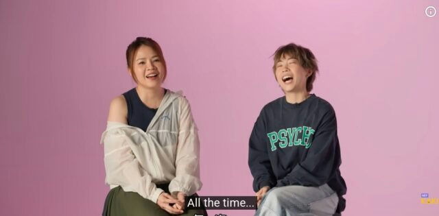 people-two women-laughing-sitting-pink background-casual clothing-subtitle