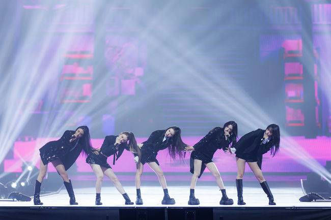people-Five K-pop idols-A-performing on stage-A-wearing black outfits and boots-B-singing into microphones-B-striking a synchronized, leaning pose-C