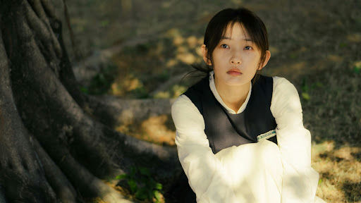people-1-young woman-A-sitting outdoors-A-white long-sleeved shirt-B-dark vest-C-large tree roots