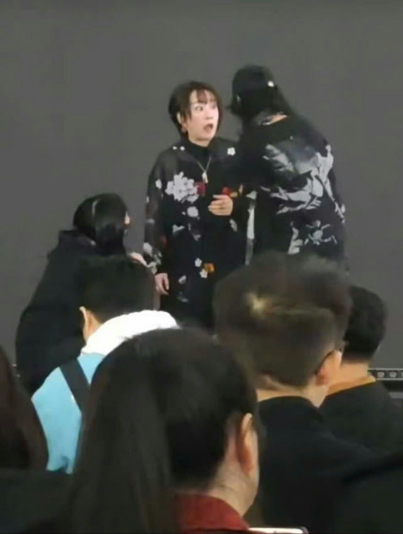 people-person with short dark hair and surprised expression-person in floral sheer top-person with dark hair leaning in-crowd in foreground