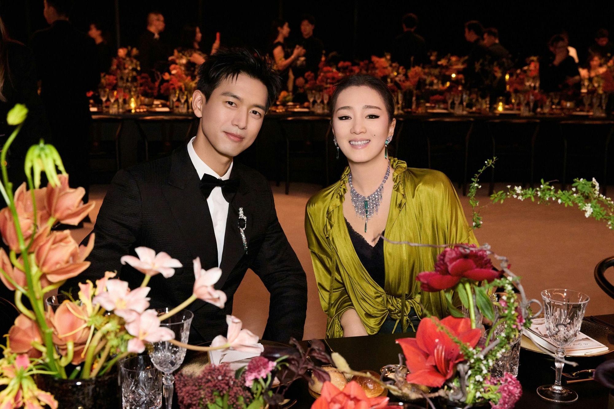 people-man and woman-formal attire-A-tuxedo and bow tie-B-olive green draped top and elaborate necklace-C-seated at a decorated dinner table