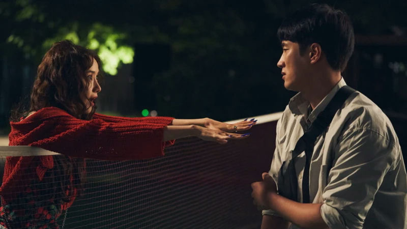 people-woman in red knit cardigan-A-man in light shirt-A-badminton net barrier-B-outdoor nighttime setting-C