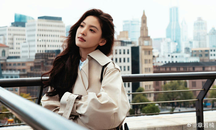 people-woman-A-long dark hair-A-wearing a beige trench coat-A-looking upwards and to the side-A-city skyline background