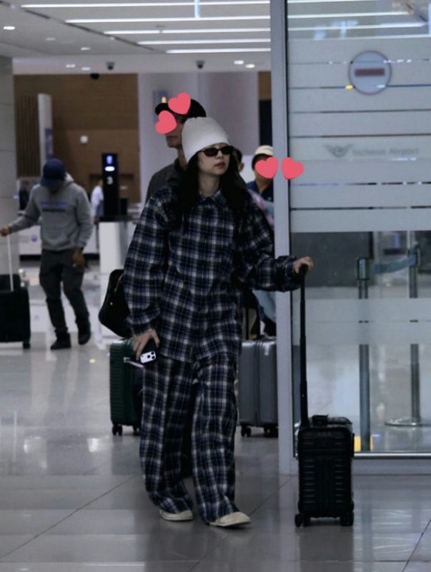 people-woman in plaid pajamas and white beanie-A-airport setting-B-person behind obscured by hearts-C-luggage visible