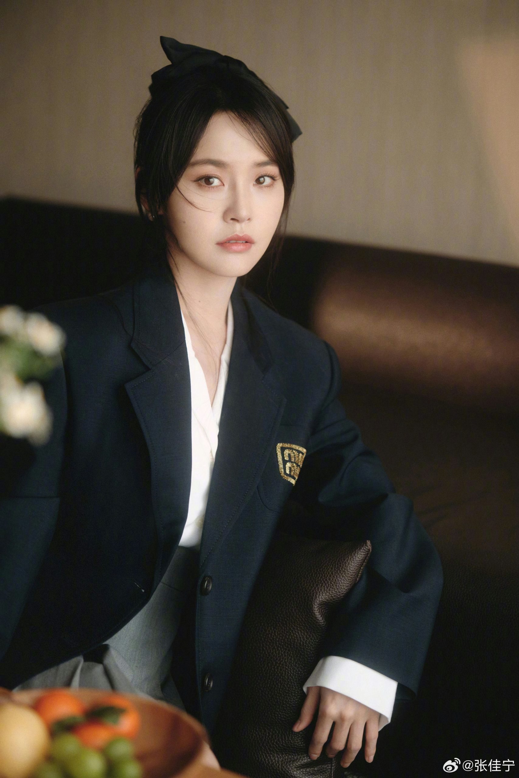 people-woman-A-dark blue blazer-B-black bow in hair-C-seated on leather sofa