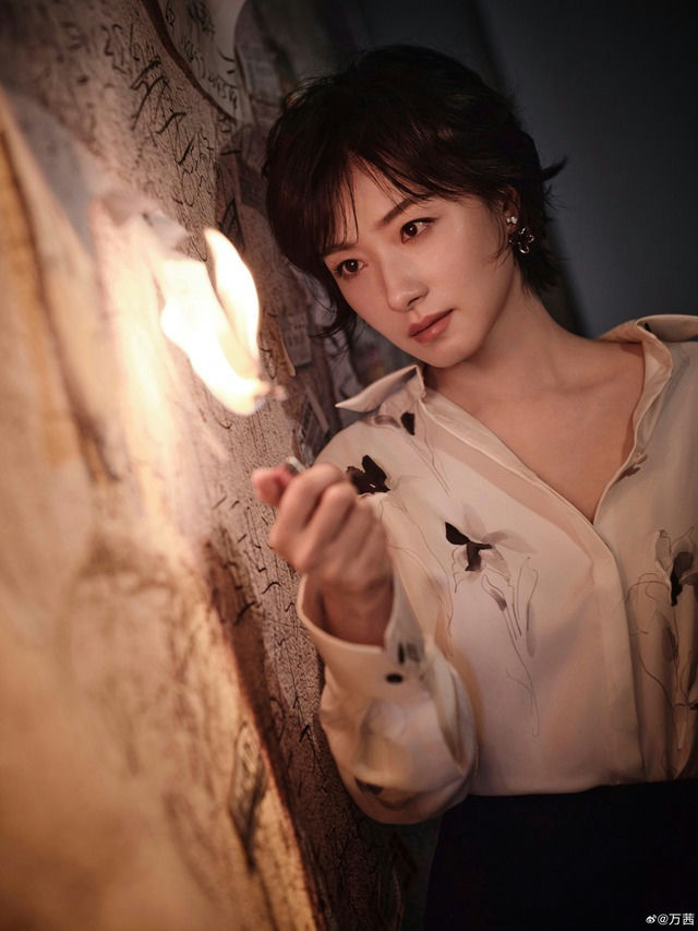 people-Woman-Short dark hair-Medium shot-Holding a lighter with flame-Leaning against a textured wall-Wearing a light-colored floral blouse
