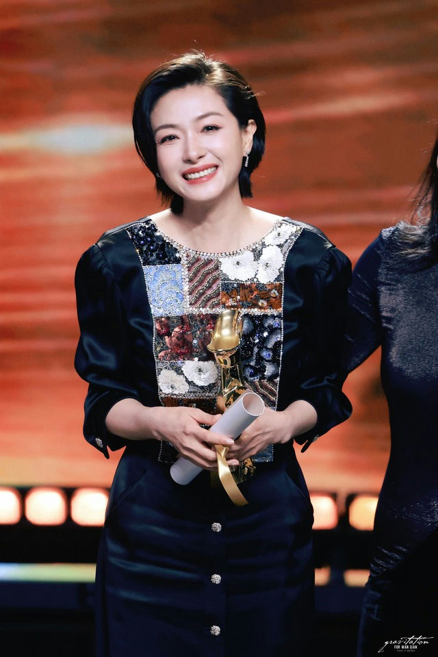 people-Woman smiling-A-holding award-B-patchwork top-C-short dark hair
