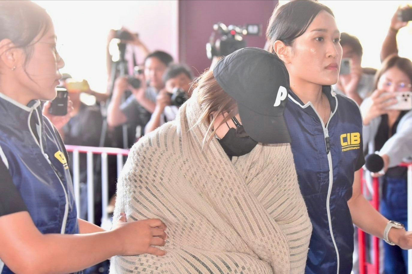 people-A-escorted individual-A-police officer-A-media scrum-A-face obscured-A-blanket-A-baseball cap