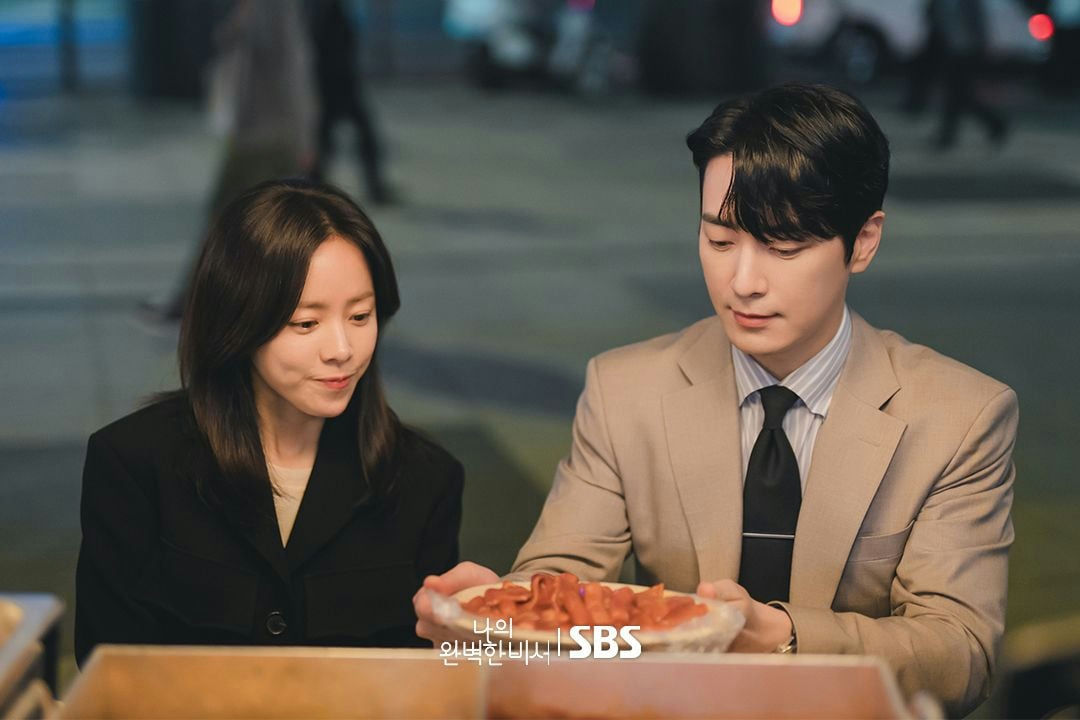 people-woman-dark hair-woman-black jacket-man-tan suit-man-holding food