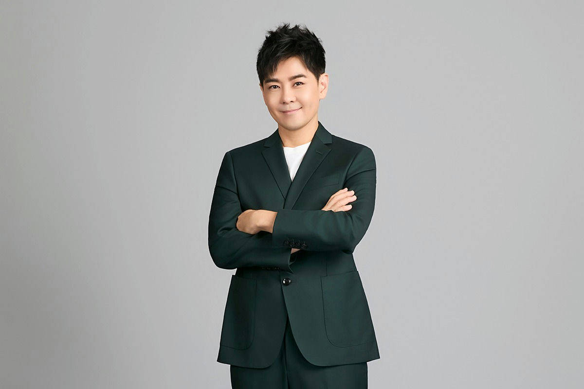 people-man-smiling-wearing-dark green suit-arms crossed-white shirt-standing against gray background
