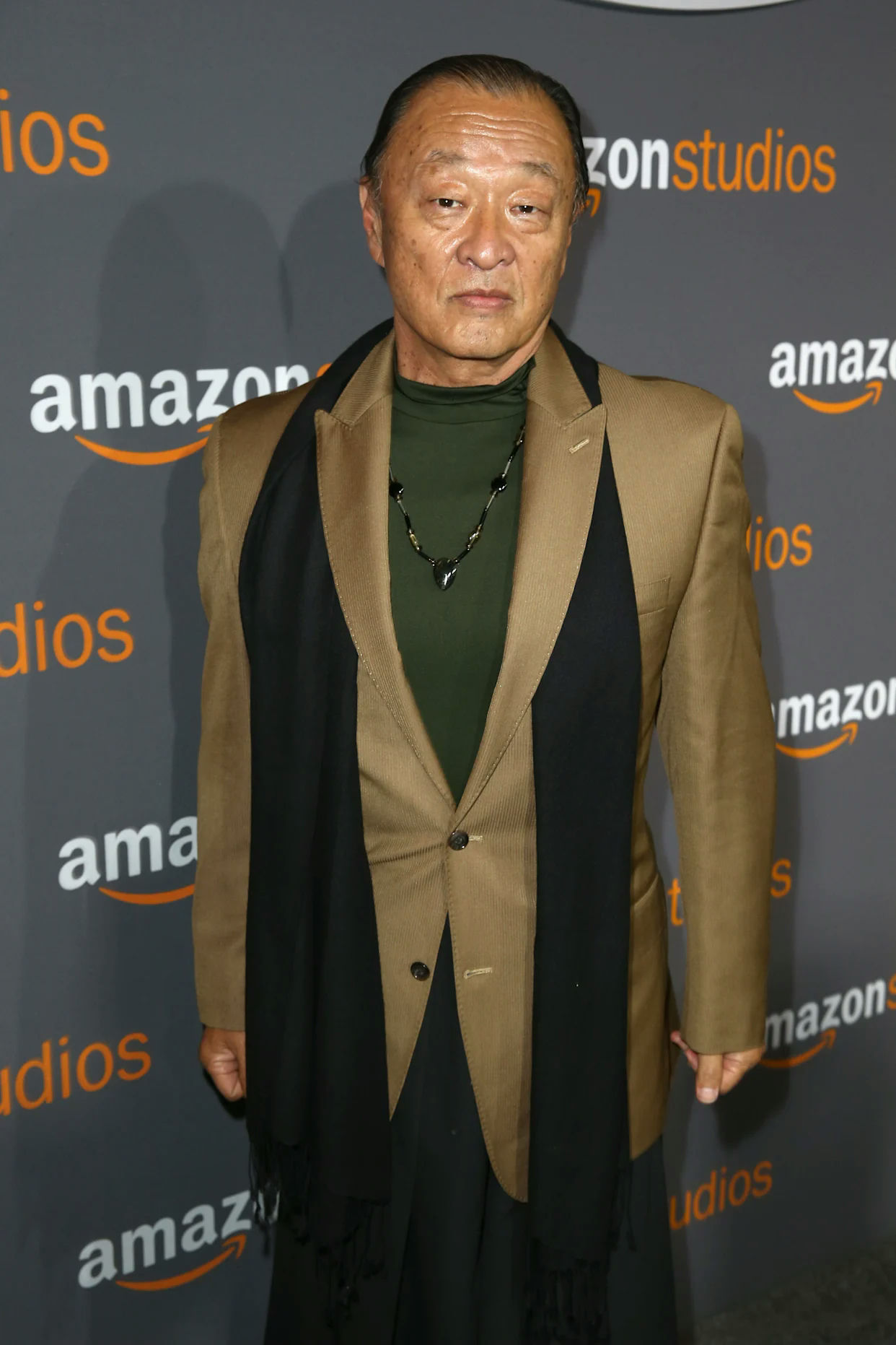 people-Cary-Hiroyuki-Tagawa-A-brown-blazer-A-black-scarf-A-green-shirt-A-Amazon-Studios-backdrop
