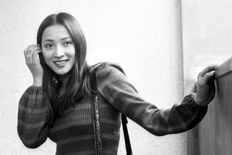people-woman-smiling-striped sweater-long dark hair-hand near ear-leaning on surface