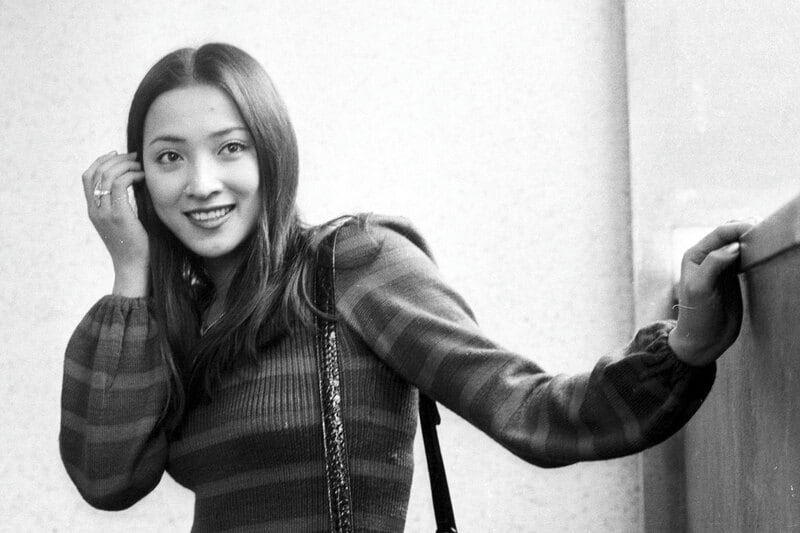 people-woman-smiling-striped sweater-long dark hair-hand near ear-leaning on surface