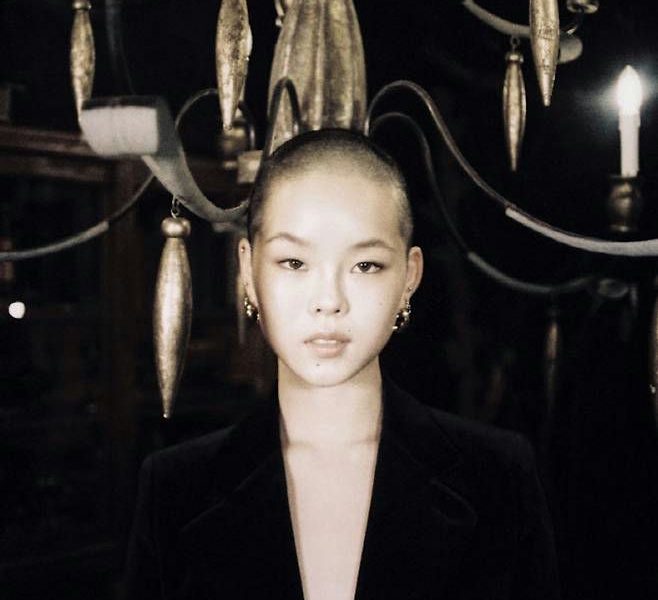 people-woman-A-shaved head-A-black jacket-A-chandelier-A-dark setting