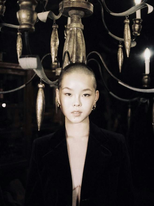 people-woman-A-shaved head-A-black jacket-A-chandelier-A-dark setting