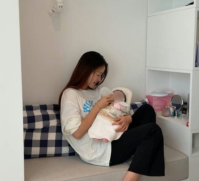people-woman-feeding a baby-baby-bottle-seating on a couch-cushion with blue and white plaid pattern
