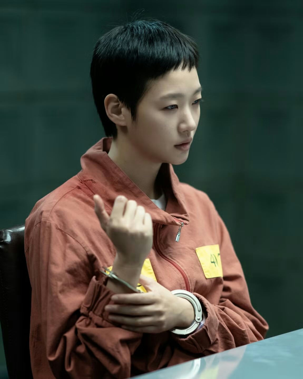 people-Young woman-A-short black hair-A-handcuffed-A-orange jumpsuit-A-serious expression