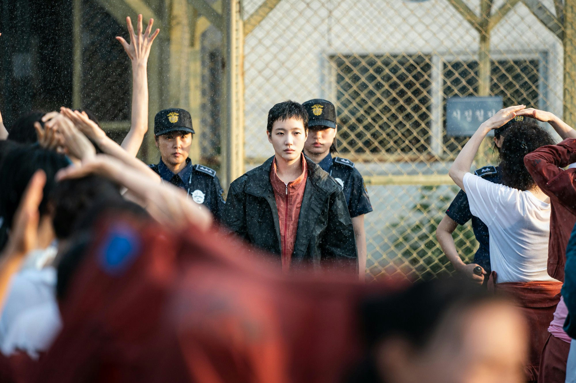 people-A-crowd-A-protest-A-water-spray-B-female-officers-B-chain-link-fence-C-central-figure-C-serious-expression