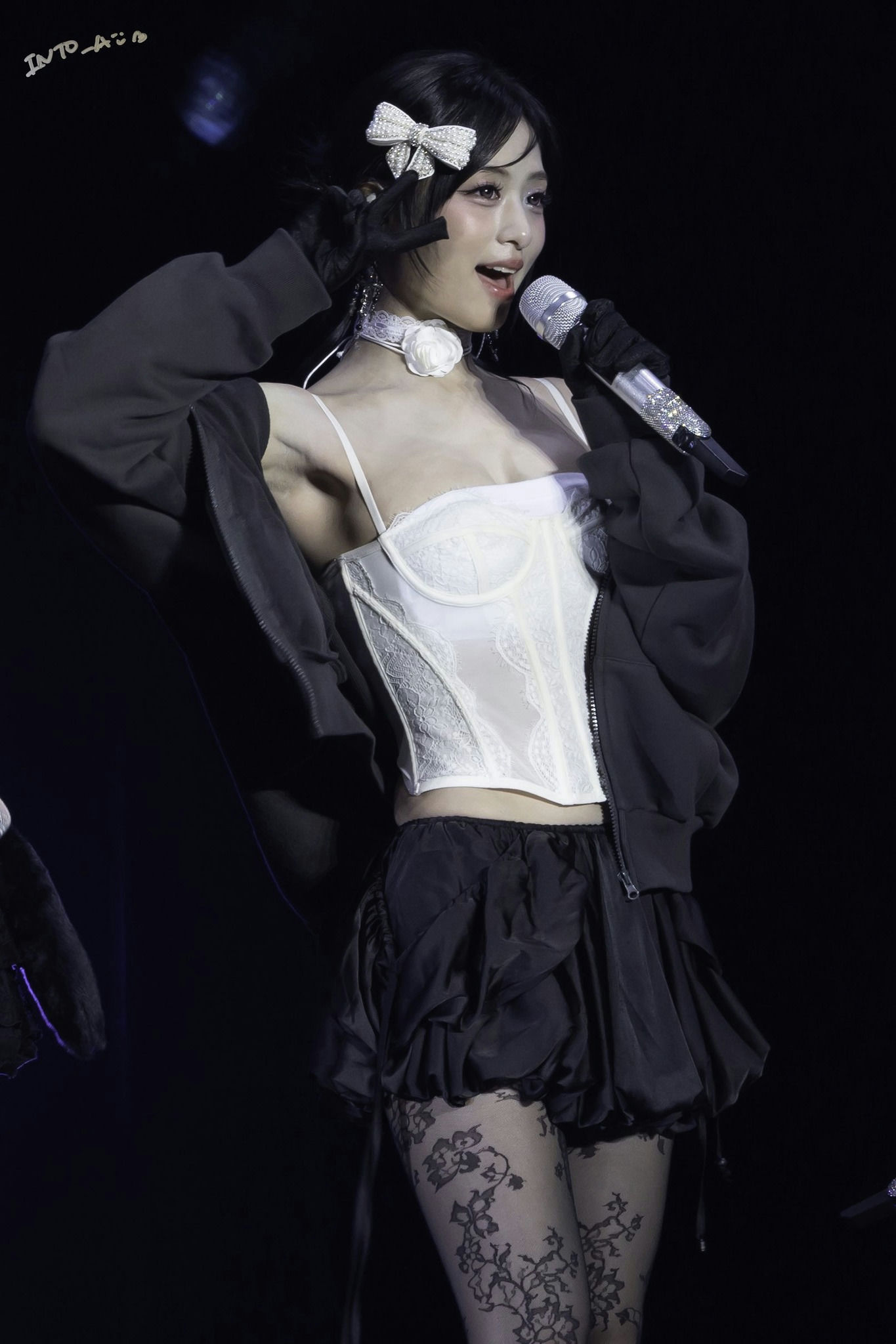 people-A-female performer-A-singing-A-white lace corset-A-black puffy skirt-A-lace patterned tights-A-black bomber jacket-A-pearl bow hair accessory-A-white floral choker