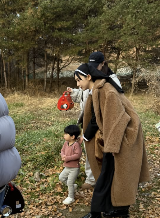 people-woman in brown teddy coat-holding red device-child in pink shirt-woman in black cap