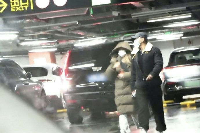people-two people-A-parking garage-A-wearing masks-A-winter clothing-B-Cadillac SUV-B-exit sign