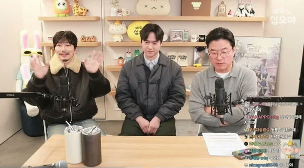 people-three men-A-sitting at a table-B-waving hello-C-in a studio setting