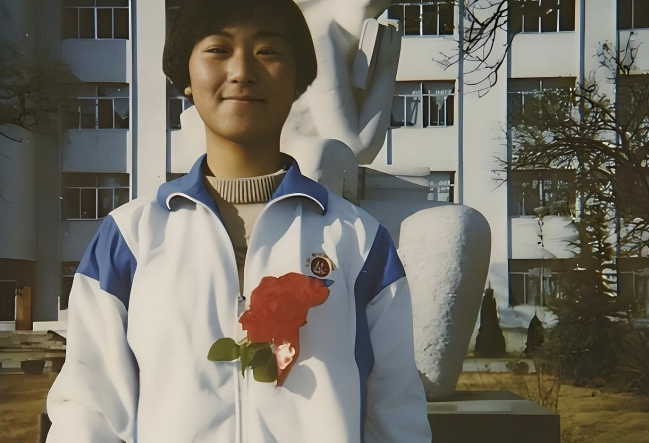 people-young Asian female student-smiling-white and blue jacket-red rose on chest-school setting-outdoor statue background