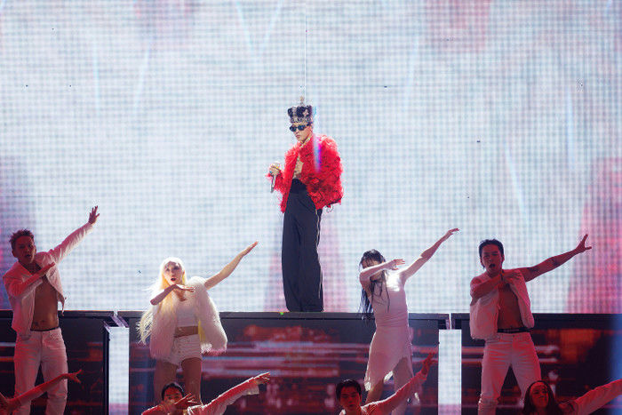 people-1-singer-A-performer-A-dancer-A-stage-performance-A-red-jacket-A-crown-A-white-outfits-A-large-screen-background