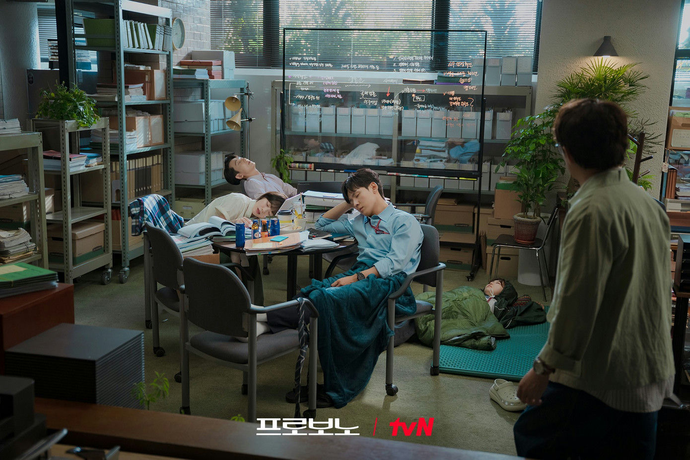 people-four people sleeping-A-office setting-A-cluttered room-B-legal documents-C-man watching-D-sleeping bag