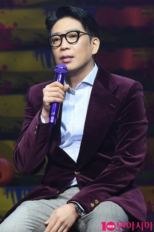 people-man-holding microphone-wearing glasses-purple velvet blazer-light blue shirt-grey patterned pants-Asia Economy Today logo