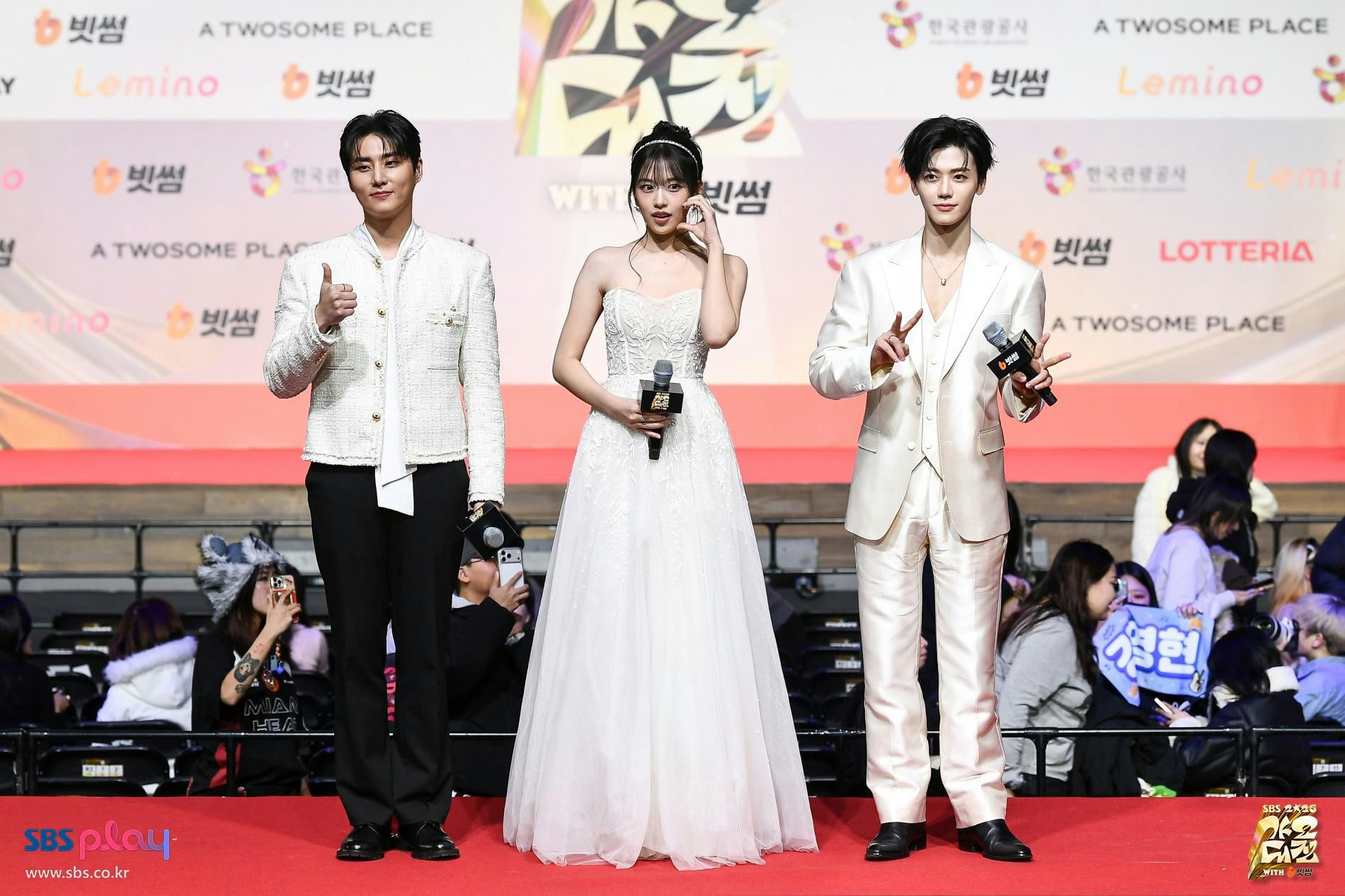 people-three-K-pop-idols-A-red-carpet-A-white-outfits-A-formal-wear-B-holding-microphones-B-posing-C-audience-watching-C