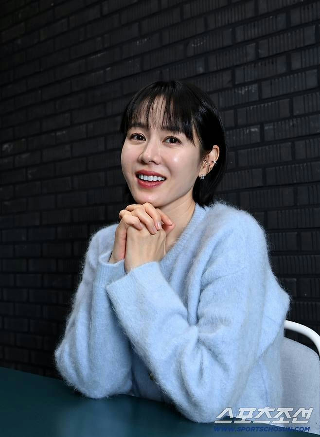 people-woman-A-smiling-A-short black hair-A-light blue fuzzy sweater-A-hands clasped