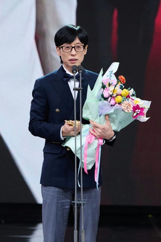 people-man-speaking at podium-holding bouquet-wearing glasses-wearing tuxedo jacket