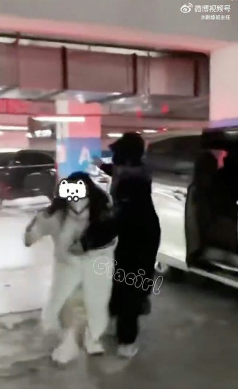 people-Two figures-A-parking garage-A-one figure wearing black-A-one figure wearing white-A-face obscured by emoji-A-interaction/movement