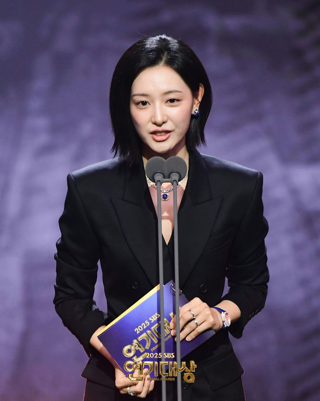 people-Woman-Award Show Presenter-Black Suit-Short Black Hair-Holding Folder-Jewelry