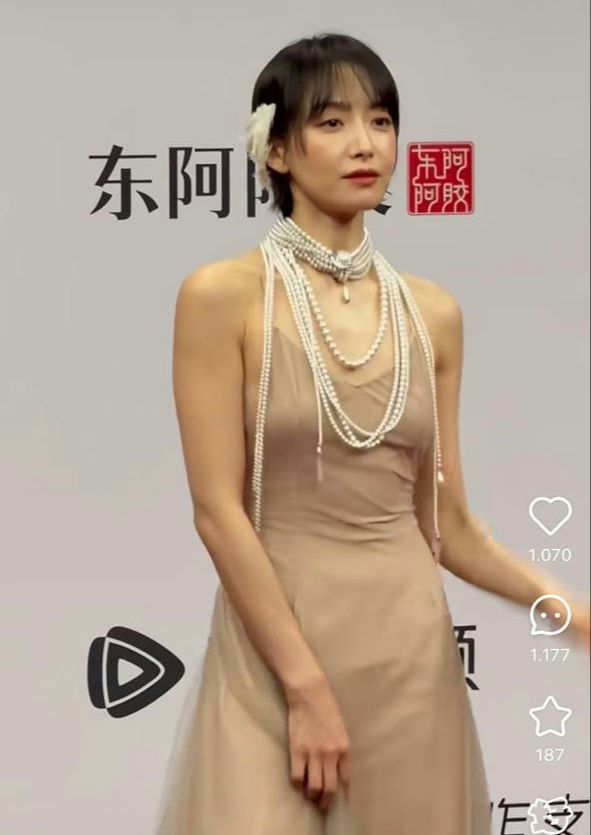 people-woman-short black hair-dress-beige sheer slip dress-jewelry-multiple layered pearl necklaces-accessory-white flower hair clip
