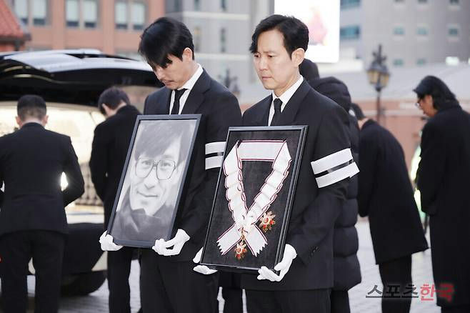 people-Lee Jung-jae-and-Park Hae-il-at-a-funeral-carrying-a-portrait-and-an-award-ribbon